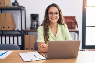 Young hispanic woman working at the office wearing glasses with a happy and cool smile on face. lucky person. 