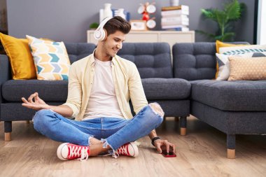 Young hispanic man doing yoga exercise sitting on floor at home