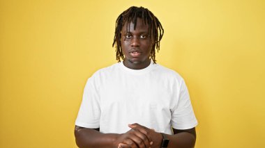 İzole edilmiş sarı arka plan üzerinde ciddi bir ifadeyle duran Afrikalı Amerikalı adam.