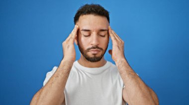 Genç Arap adam izole edilmiş mavi arka plan yüzünden baş ağrısı çekiyor.