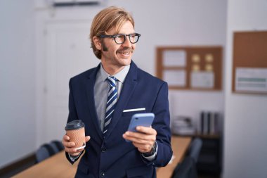 Genç sarışın iş adamı akıllı telefon kullanıyor ofiste kahve içiyor.