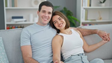 Güzel bir çift kanepede oturmuş birbirlerine sarılıyor ve gülümsüyor.