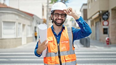 Genç İspanyol mimar. İnşaat alanının planlarını elinde tutarak gülümsüyor.
