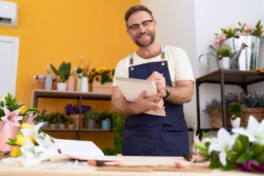 Middle age man florist smiling confident writing on notebook at flower shop