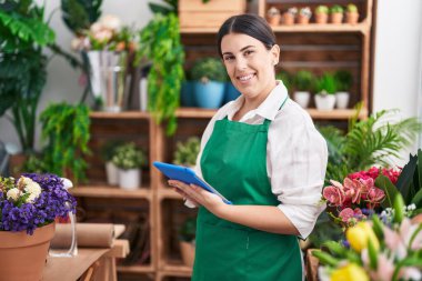 Young beautiful hispanic woman florist smiling confident using touchpad at flower shop