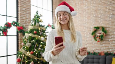 Genç sarışın kadın Noel 'i evde akıllı telefon kullanarak kutluyor.