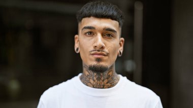 Sokakta ciddi bir ifadeyle dikilen genç Latin adam.