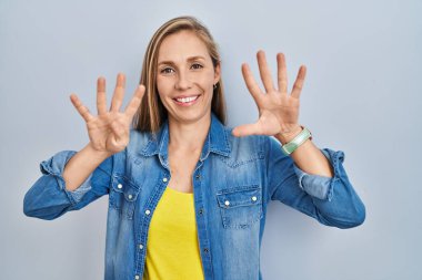 Mavi arka planda duran genç sarışın kadın dokuz numarayı gösterip işaret ederken kendinden emin ve mutlu bir şekilde gülümsüyor.. 