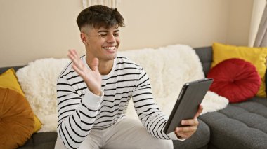 Çekici, genç İspanyol bir adam evdeki kanepede rahatça oturuyor, eğlenceli bir video görüşmesi yaparken mutluluktan parlıyor.