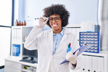 Afrikalı Amerikalı bilim kadını gülümsüyor. Laboratuvarda elinde bir pano var.