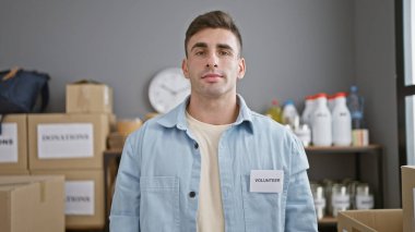 Yakışıklı, İspanyol asıllı, ciddi bir yüzle gönüllü bir adam, bağış kutularının arasında bir hayır kurumunda duruyor, toplumu desteklemek için çok çalışıyor..