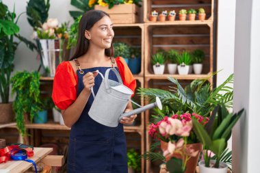 Young beautiful hispanic woman florist watering plant at florist