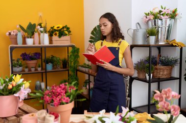 Young african american woman florist writing on notebook standing at flower shop