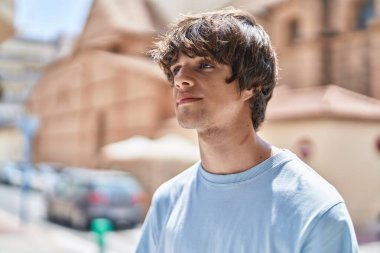 Sokakta ciddi bir ifadeyle yan tarafa bakan genç sarışın adam.