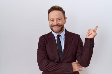 Orta yaşlı iş adamı, sakallı, takım elbiseli, kravatlı, yüzünde kocaman bir gülümseme olan, el parmağı ile kameraya bakan.. 