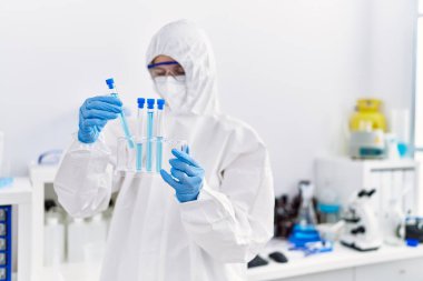 Laboratuvarda test tüpleri tutan güvenlik üniforması giyen genç sarışın bilim kadını.