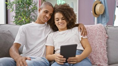 Gündelik ama kendine güvenen güzel çift evdeki kanepede birlikte oturup, gülerek ve gülerek dokunmatik dokunmatik zeminde gezinirken eğlenceli anların tadını çıkarıyor.