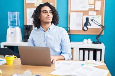 Ofiste çalışan genç Latin bir iş adamı dizüstü bilgisayar kullanıyor.