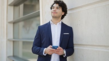 Sokakta gülümseyen akıllı telefon kullanan genç Latin iş adamı.