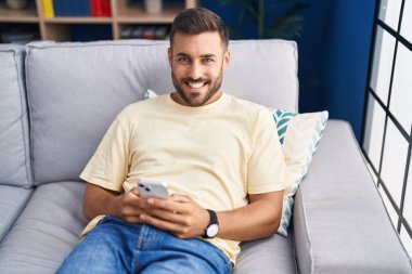 Evdeki kanepede oturan, akıllı telefon kullanan genç bir İspanyol.