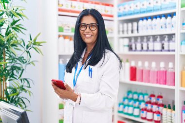 Eczanede çalışan akıllı telefon kullanan orta yaşlı İspanyol kadın eczacı.