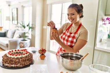 Genç ve güzel İspanyol kadın gülümsüyor. Mutfakta kekin üstüne çilek koyuyor.