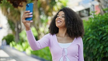 Afro-Amerikalı kadın, parkta akıllı telefonun yanında kendinden emin bir şekilde selfie çekiyor.