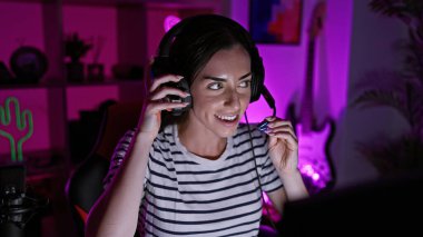 Çekici, genç İspanyol kadın, gülümseyen ve kendinden emin, oyun macerasını yaşıyor, karanlık bir gecede oyun odasında kulaklık takıyor, sanal bir dünyada büyüleniyor.