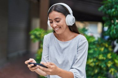 Genç ve güzel İspanyol kadın gülümsüyor. Sokakta akıllı telefondan videolar izliyor.