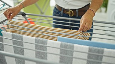 Orta yaşlı İspanyol kadın çamaşırhanede çamaşır ipine elbise asıyor.