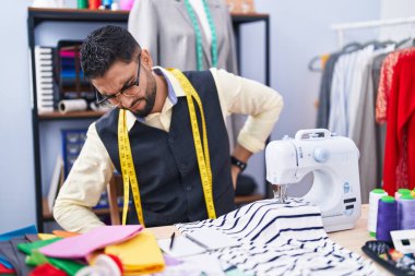 Young arab man tailor stressed using sewing machine at clothing factory