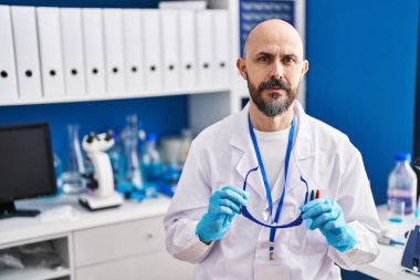 Laboratuvarda güvenlik gözlüğü tutan kel bir bilim adamı.