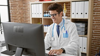 Genç İspanyol doktor klinikte gülümseyen bilgisayar kullanıyor.