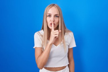 Mavi arka planda dikilen beyaz bir kadın sessiz olmak istiyor. sessizlik ve gizli konsept. 