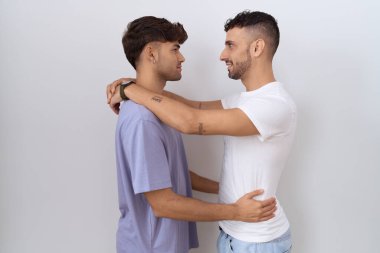 Homoseksüel eşcinsel çift beyaz arka planda duruyor. Yan tarafa bakıyor, rahat bir poz veriyor ve kendine güvenen bir gülümseme sergiliyor.. 