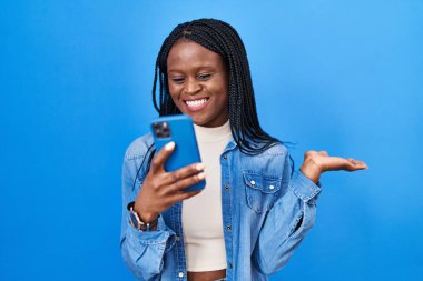 Örgülü Afrikalı bir kadın akıllı telefon kullanarak zaferi mutlu bir gülümsemeyle ve ellerini kaldırarak kutluyor. 