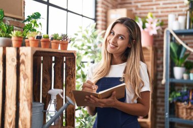 Young blonde woman florist smiling confident writing on notebook at florist clipart