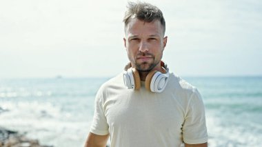 Sahilde ciddi bir ifadeyle duran, kulaklık takan genç bir adam.