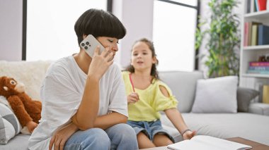 Anne ve kız kanepede çizim üzerine bağ kurar, anne cep telefonu konuşmasını dengeler ve evde aile zamanını dengeler.