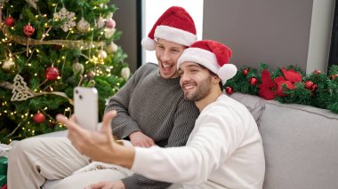 Noel 'i kutlayan iki erkek evde akıllı telefondan selfie çekiyor.