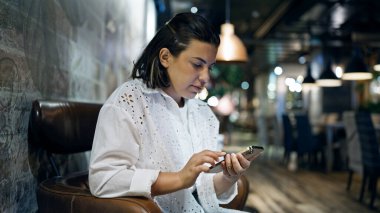 Kafeteryada akıllı telefon kullanan güzel, genç bir İspanyol kadın.