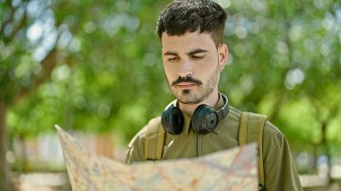 Sırt çantası ve kulaklık takan İspanyol turist parkta harita arıyor.
