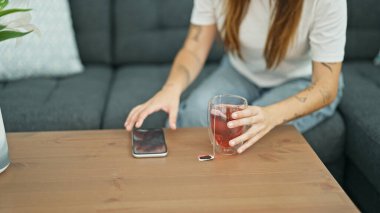 Genç, güzel, İspanyol bir kadın elinde akıllı telefon ve bir bardak çay ile caddedeki kanepede oturuyor.