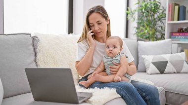 Anne ve kızının gündelik bağ kurma seansı, kanepede oturmak, rahat evlerinde dizüstü bilgisayar ve akıllı telefon aracılığıyla çevrimiçi sohbetler yapmak.