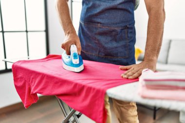 Orta yaşlı, kır saçlı, evde giysilerini ütüleyen bir adam.