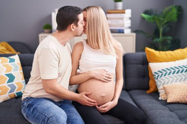 Kadın ve erkek bebek bekliyor. Birbirlerine sarılıyorlar. Evde öpüşüyorlar.