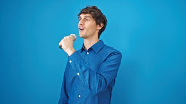 Genç İspanyol adam mavi arka planda şarkı söyleyerek müzik dinliyor.