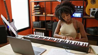 Müzik stüdyosunda dizüstü bilgisayar kullanarak piyano çalan Afrikalı Amerikalı kadın müzisyen.