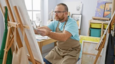 Yakışıklı, orta yaşlı, beyaz bir adam. Kapalı mekan sanat stüdyosunda tutkuyla bir portre çizerken son derece konsantre olan bir sanatçı.