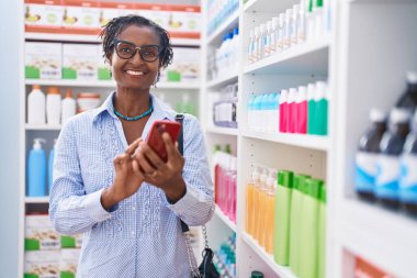 Orta yaşlı Afro-Amerikan kadın müşteri eczanede akıllı telefon kullanarak gülümsüyor.